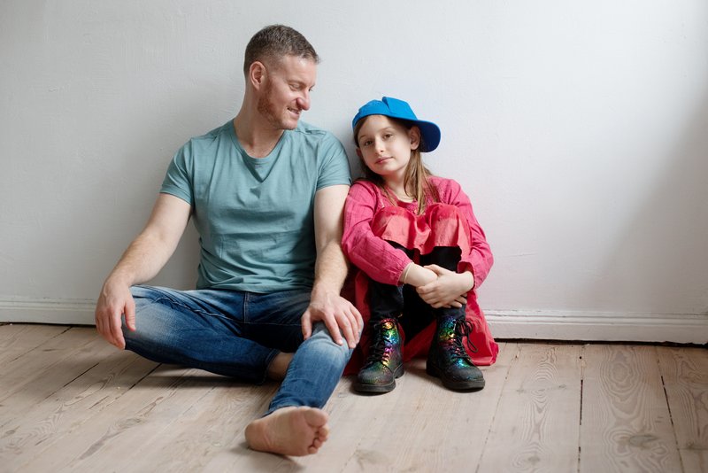 Ein Mann sitzt mit einem Kind vor einer Zimmerwand auf dem Boden