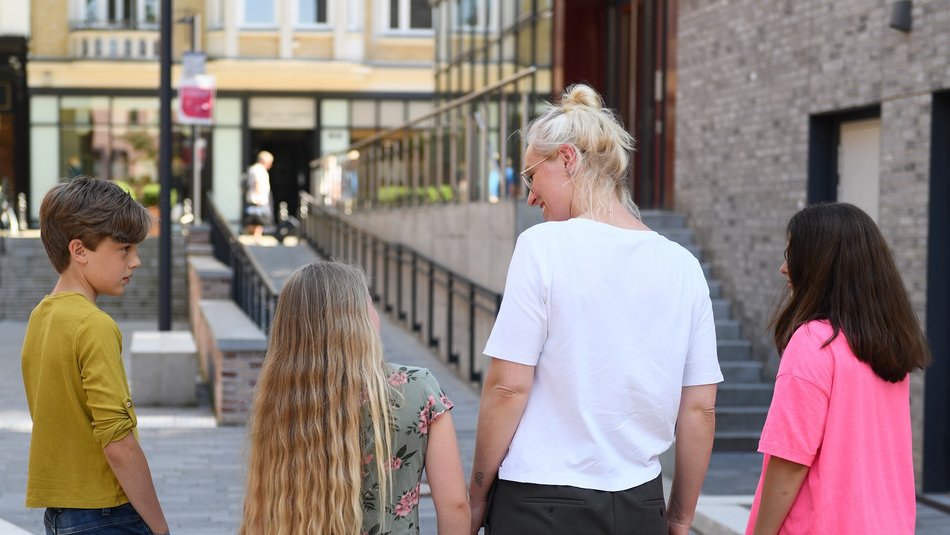 Drei Kinder, eine erwachsene Person von hinten in einerAltstadtkulisse
