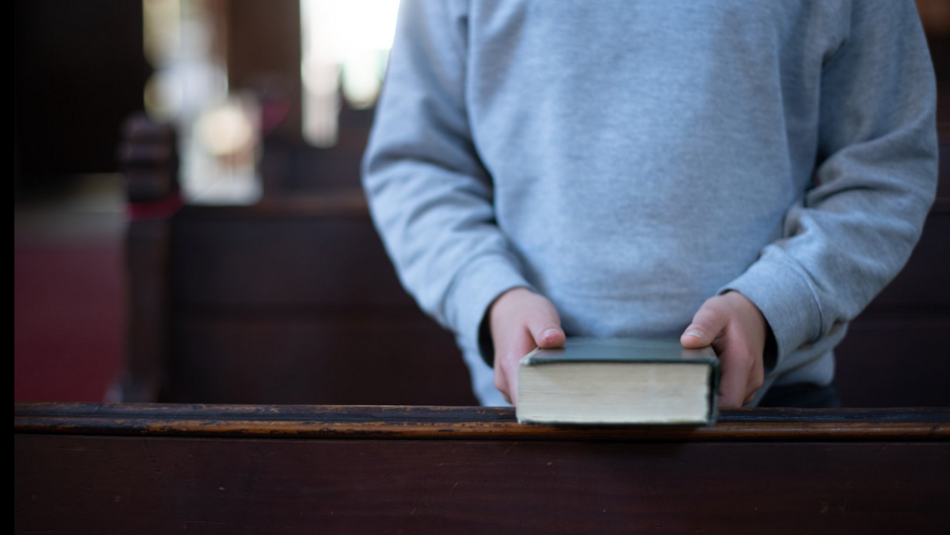 Person mit einer Bibel in der Hand steht vor einer Kirchenbank