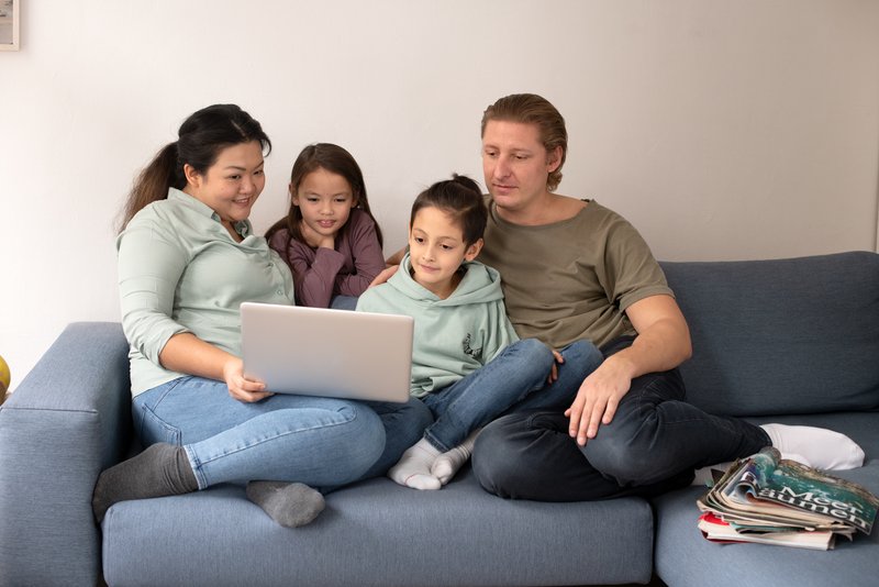Eine Familie sitzt auf einer Couch und schaut gemeinsam auf den Bildschirm eines Laptops