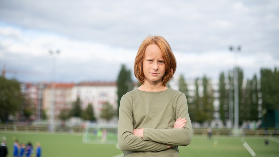 Ein Junge steht mit verschränkten Armen vor einem Fußballfeld