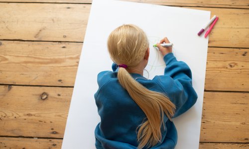 Ein Kind liegt auf einem großen Blatt Papier auf dem Boden und malt 