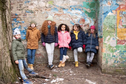 Sechs Kinder und Jugendliche lehnen in einer Mauernische, von der der Putz und bunte Farbe abblättert