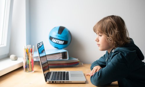Ein Junge sitzt vor einem Laptop und schaut auf den Display