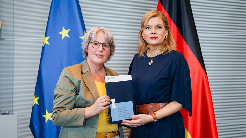 Kerstin Claus (links) überreicht Julia Klöckner (rechts) einen Bericht vor einer Deutschland- und EU-Flagge