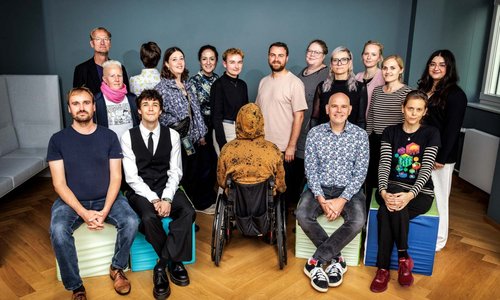 Gruppenbild der 17 Mitglieder des Betroffenenrates bei der Unabhängigen Bundesbeauftragten gegen sexuellen Missbrauch von Kindern und Jugendlichen, die sitzend und stehend in regelmäßigem Abstand in die Kamera blicken, zwei Menschen stehen mit dem Rücken zur Kamera