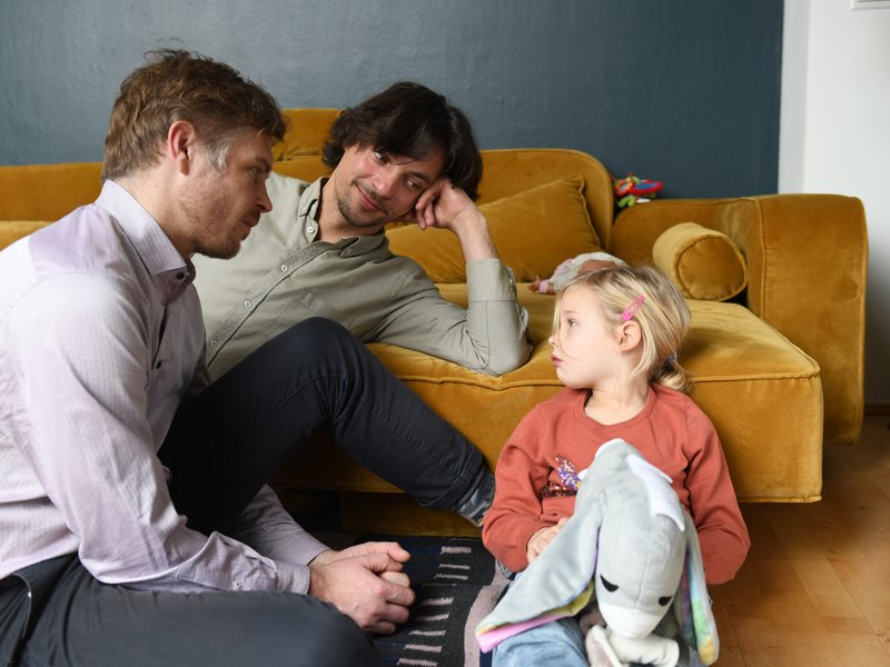 Väter und Kind sitzen vor einem Sofa auf dem Boden 