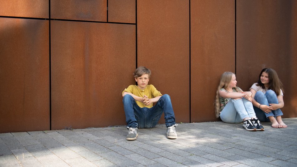 Ein Junge und zwei Mädchen sitzen vor einer Wand