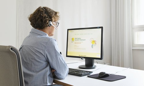 Frau sitzt vor einem Computer am Schreibtisch. Auf dem Desktop sieht man die Website www.hilfe-telefon-missbrauch.de 